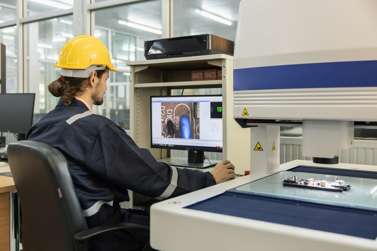 Opérateur en atelier lisant le relevé d'une machine de mesure optique sur son écran de contrôle